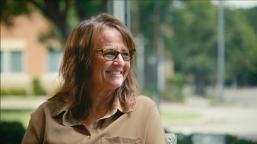 Smiling woman with glasses outdoors, looking to the side on a sunny day.