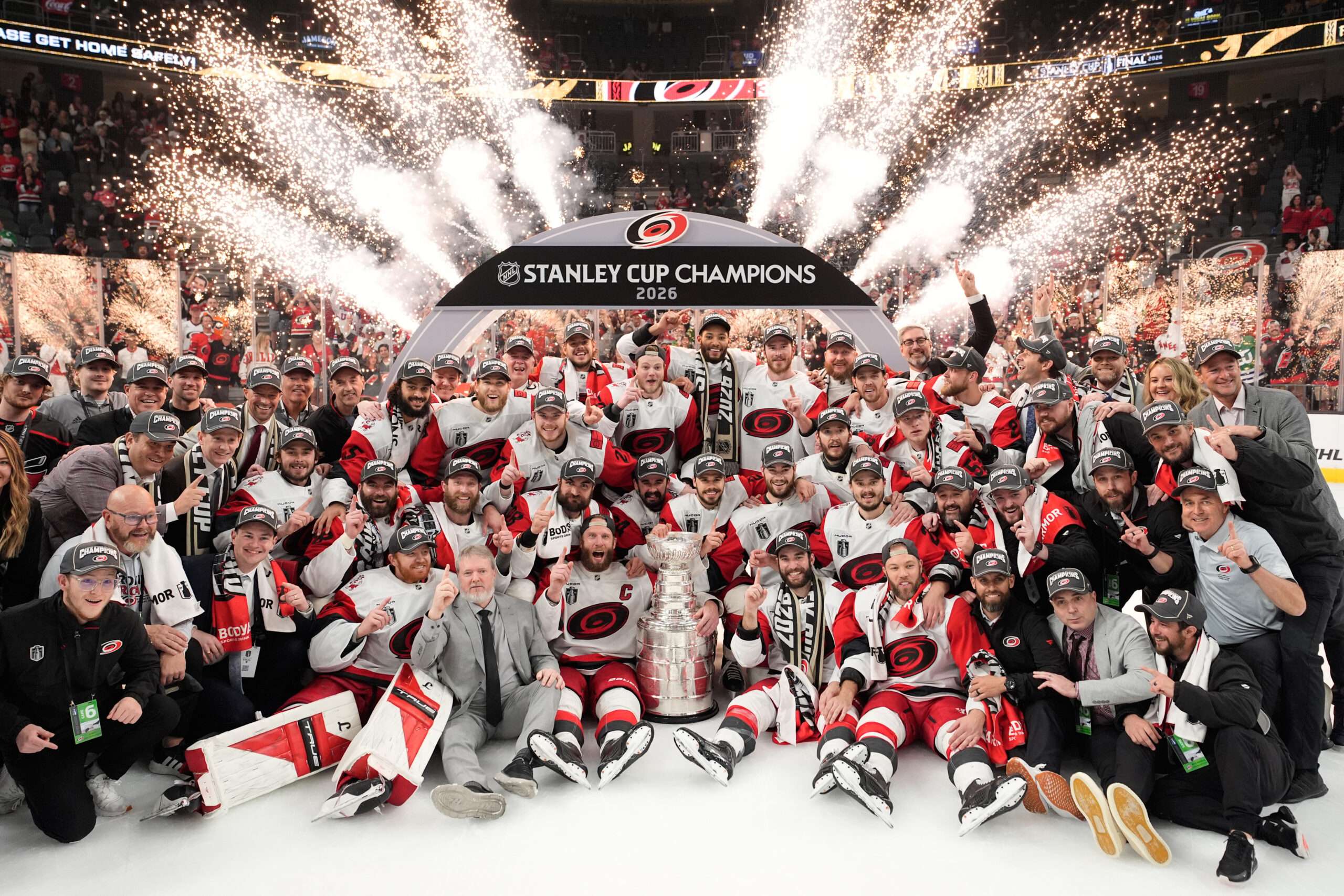 Hockey team posing with the Stanley Cup as fireworks explode behind them on the ice.